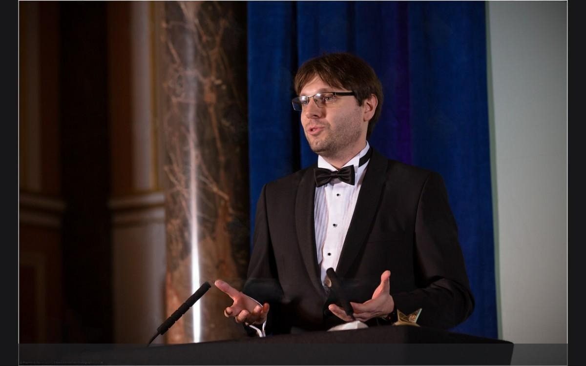 Karol Chlasta speaking at a lectern in black tie during the awards dinner
