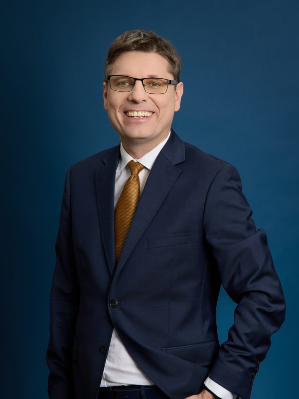 Karol Chlasta, standing portrait in a navy suit against a navy backdrop